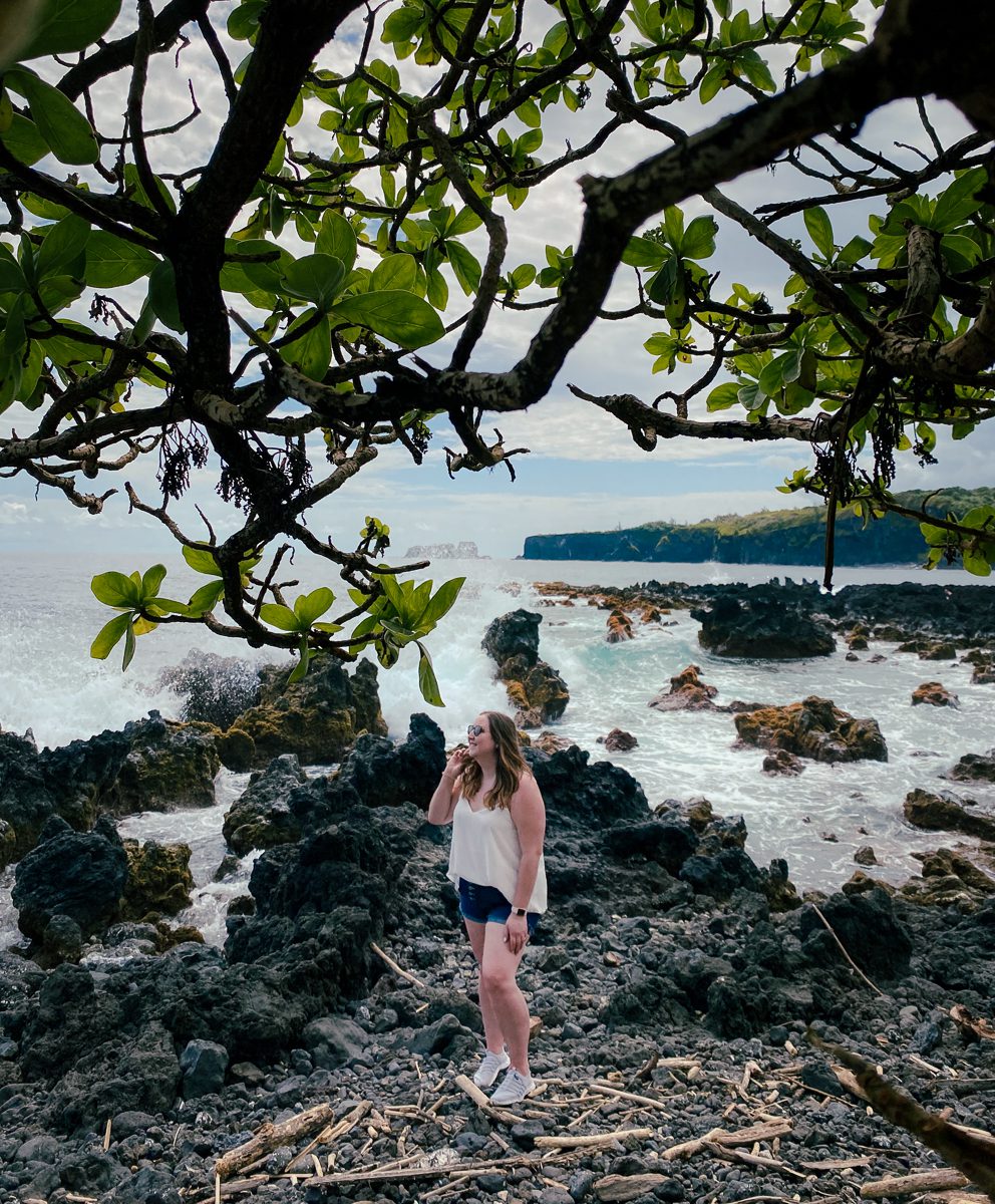 Woman standing on Keanae Peninsula with wave crashing in behind